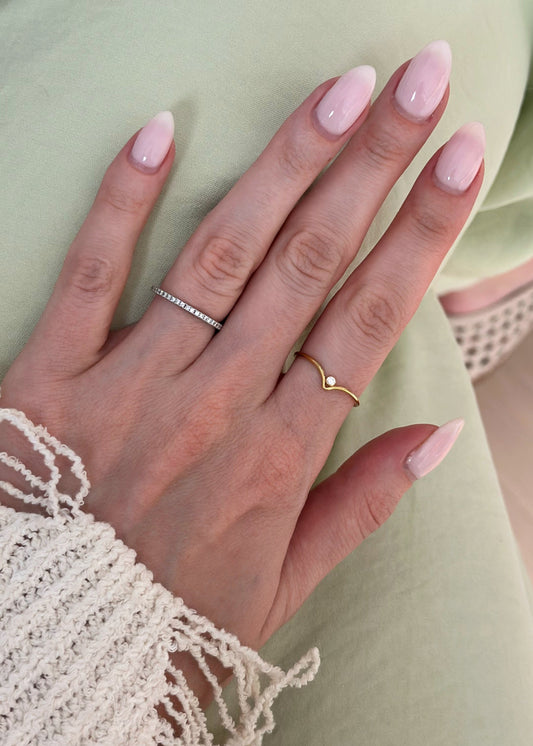 Close-up of a hand with pink nail polish wearing two rings against a light green background