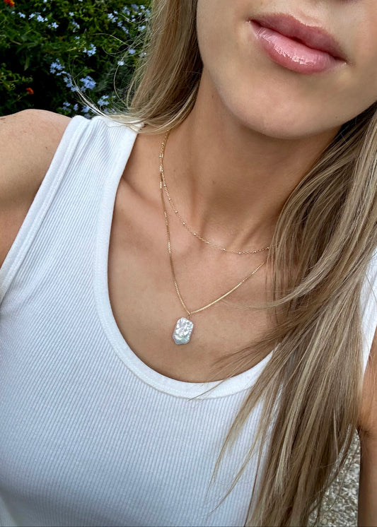 model wearing a gold filled necklace with a baroque pearl layered with a mixed metal gold and silver satellite necklace