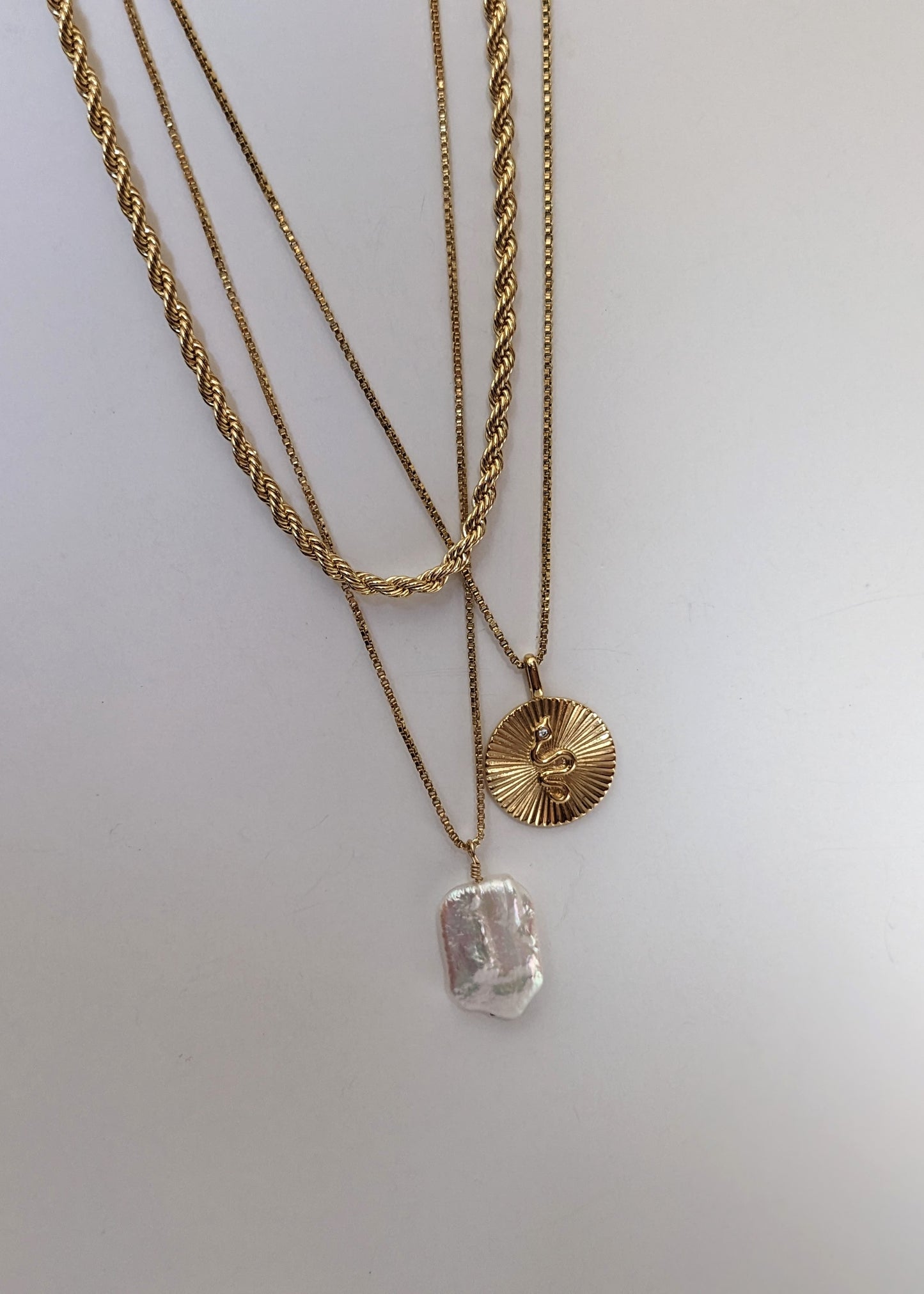 a gold filled necklace with a baroque pearl layered with a gold rope chain and snake pendant necklace