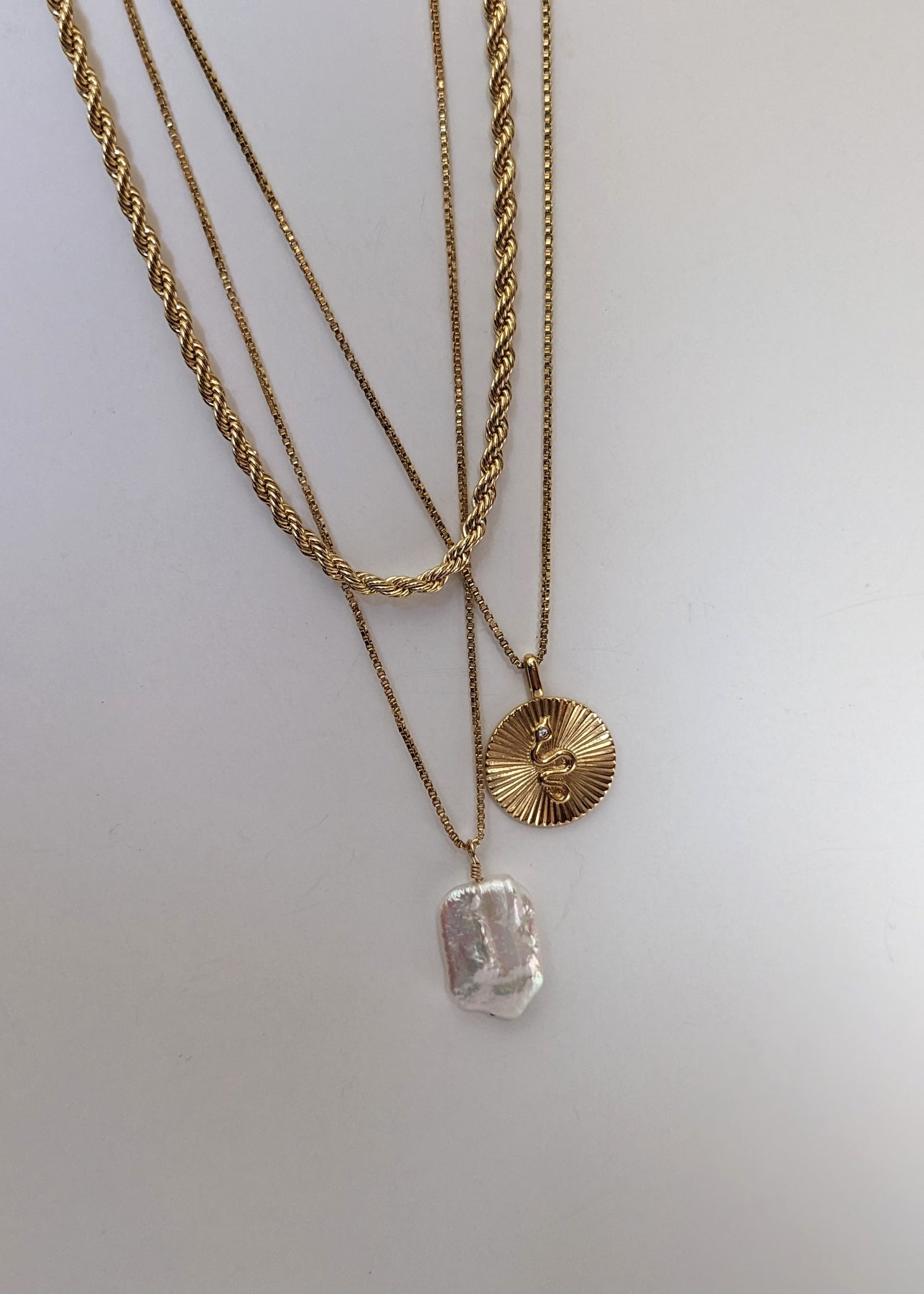 a gold filled necklace with a baroque pearl layered with a gold rope chain and snake pendant necklace